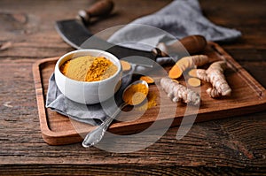 Anti-inflammatory food ingredient, turmeric powder in a ceramic bowl and fresh root on wooden background