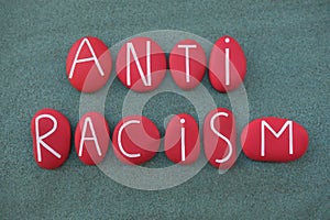 Anti Racism, social issue slogan text composed with red colored stone letters over green sand photo