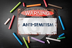 Anti-Semitism. Metal warning sign and colored pieces of chalk on a dark chalkboard background