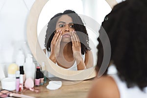 Anti-Wrinkle Skincare. Upset Black Woman Touching Her Face, Looking In Mirror