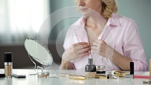 Anti-wrinkles products on table with senior woman looking neck in mirror, beauty