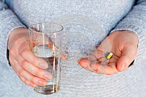 Antibiotic pills, contraceptives and a glass of water in the hands of a young woman close-up