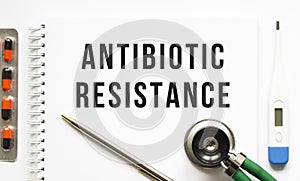 ANTIBIOTIC RESISTANCE is written in a notebook on a white table next to pills and a stethoscope