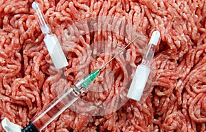 Antibiotic use in food producing animals concept: two white ampules, syringe and injection needle with minced raw meat background