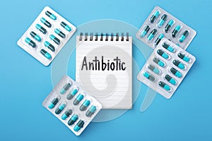 Antibiotic word on notebook with capsule pills in pack on blue background