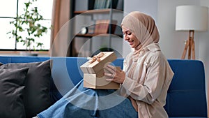 Anticipate smiling Saudi woman opening festive gift box celebrating holiday with positive emotion