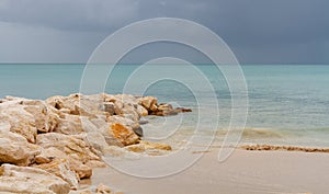 Antigua beach and rock jetty with gentle waves and storm clouds on calm sea