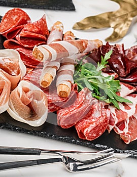 Antipasto platter cold meat with grissini bread sticks, prosciutto, slices ham, beef jerky, salami on slate stone board