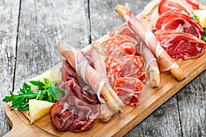 Antipasto platter cold meat plate with grissini bread sticks, prosciutto, slices ham, beef jerky, salami and arugula