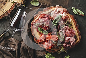 Antipasto platter cold meat plate with prosciutto, slices ham, salami, decorated with basil and olive on dark wooden background