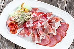 Antipasto platter cold meat plate with prosciutto, slices ham, salami, decorated with physalis and slices of melon