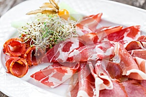 Antipasto platter cold meat plate with prosciutto, slices ham, salami, decorated with physalis and slices of melon