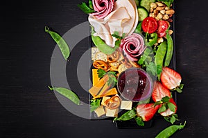 Antipasto platter cold sliced ham, salami, crackers, strawberries, vegetables and cheese platter on  board over dark background.