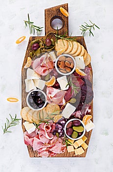 Antipasto platter with ham, prosciutto, salami, cheese, crackers and olives on a light background.