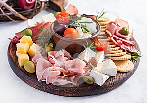 Antipasto platter with ham, prosciutto, salami, cheese, crackers and olives on a light background.