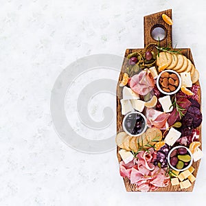 Antipasto platter with ham, prosciutto, salami, cheese, crackers and olives on a light background.