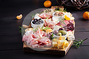 Antipasto platter with ham, prosciutto, salami, cheese, crackers and olives on a wooden background.