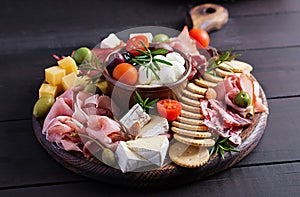 Antipasto platter with ham, prosciutto, salami, cheese, crackers and olives on a wooden background.