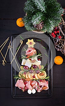Antipasto platter with ham, prosciutto, salami, cheese, crackers and olives on a wooden background.