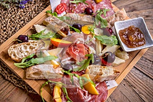 Antipasto platter with ham, prosciutto, salami, cheese, crackers and olives on a wooden background