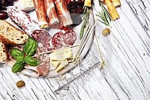 Antipasto various appetizer. Cutting board with prosciutto, salami, cheese, bread and olives on white wooden background