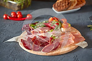 Antipasto on a wooden plate close-up. Cold smoked meat plate with sliced ham, prosciutto, and bacon. Decorated with