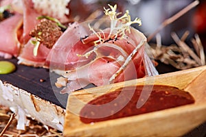 Antipasto on wooden plate close up. Cold smoked meat plate with tomato hot sauce, sliced ham, prosciutto, bacon