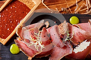 Antipasto on wooden plate close up. Cold smoked meat plate with tomato hot sauce, sliced ham, prosciutto, bacon