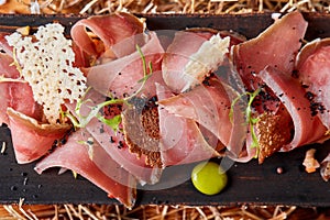 Antipasto on wooden plate close up. Cold smoked meat plate with tomato hot sauce, sliced ham, prosciutto, bacon