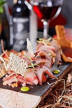 Antipasto on wooden plate close up. Cold smoked meat plate with tomato hot sauce, sliced ham, prosciutto, bacon