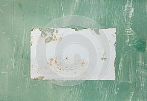 An antique aged sign with green textured paint and a white rectangle blank area in the middle.