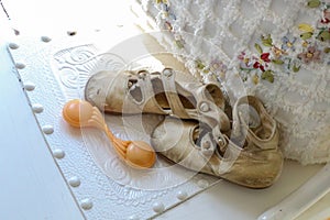 Antique baby shoes and rattle by floral and fringed pillow