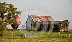 Antique barn in a field with a colorful hot air balloon