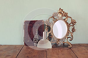 Antique blank Victorian style frame and old book with vintage necklace on wooden table. retro filtered image