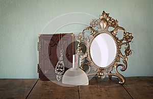Antique blank Victorian style frame and old book with vintage necklace on wooden table. retro filtered image