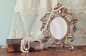 Antique blank victorian style frame and old book with vintage pearl necklace on wooden table. retro filtered image