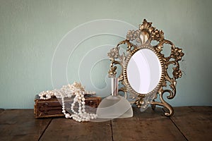 Antique blank Victorian style frame and old book with vintage pearl necklace on wooden table. retro filtered image