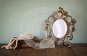 Antique blank Victorian style frame and old book with vintage pearl necklace on wooden table. retro filtered image