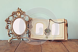 Antique blank victorian style frame and old open photograph album on wooden table. retro filtered image.