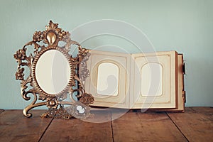 Antique blank victorian style frame and old open photograph album on wooden table. retro filtered image.