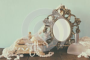 Antique blank victorian style frame, perfume bottle and white pearls on wooden table. retro filtered and toned