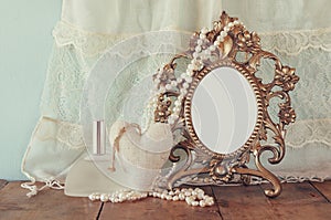 Antique blank victorian style frame, perfume bottle and white pearls on wooden table. retro filtered and toned