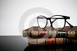 Antique books and reading glasses on a reflective surface. Daylight