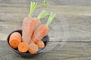 Antique bowl with fresh carrots and cut on wooden table, closeup