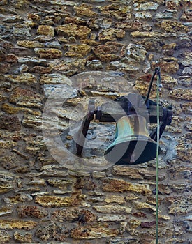 Antique Brass Bell Hanging in a Victorian Garden. Brass Bell on a Stone Wall in the Old Style
