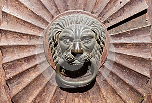 Antique brass door knocker in the shape of a lion`s head, detail of metal door