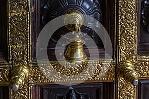 Antique bronze bell on a wooden door with inlaid Hindu temple.