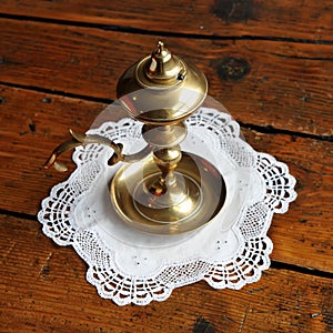 Antique bronze oil candlestick on a white embroidered cloth and antique wooden table.