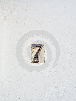 Antique ceramic tile number 7 on a whitewashed wall