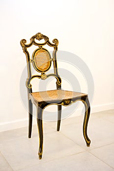 An antique chair in black and gold stands against the wall